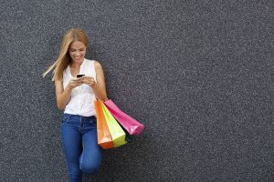 Happy young woman typing a message the phone after shopping