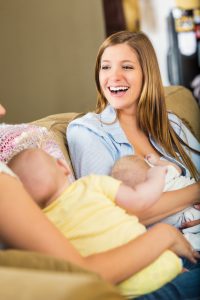 Young adult Caucasain women are sitting together while holding babies. Mothers are breastfeeding their children during a breastfeeding support group meeting with local lactation counselor or consultant.
